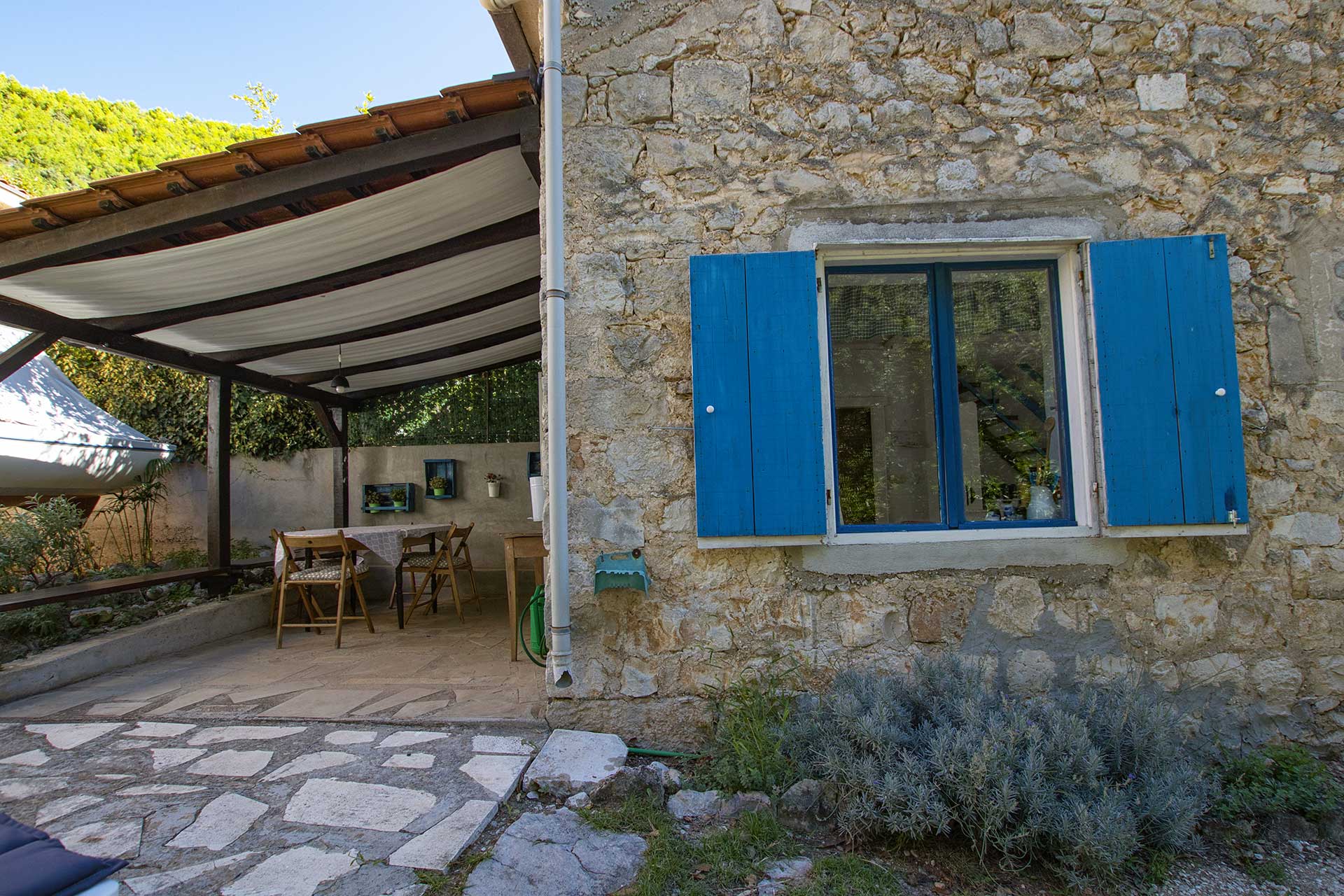 Stone front of the cottage with blue shutters and the covered terrace